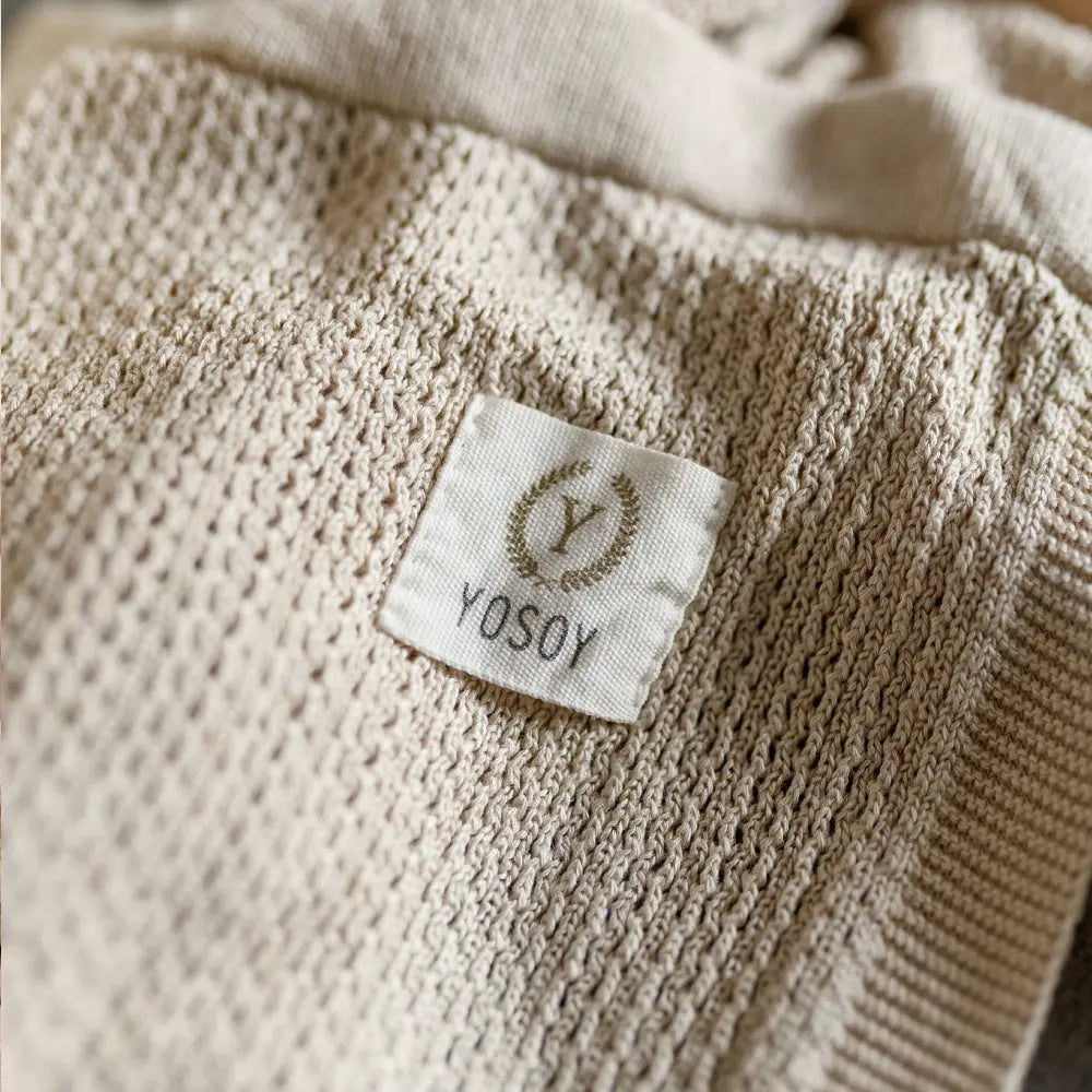 Zbliżenie na metkę z logo YOSOY na beżowej dzianinie.