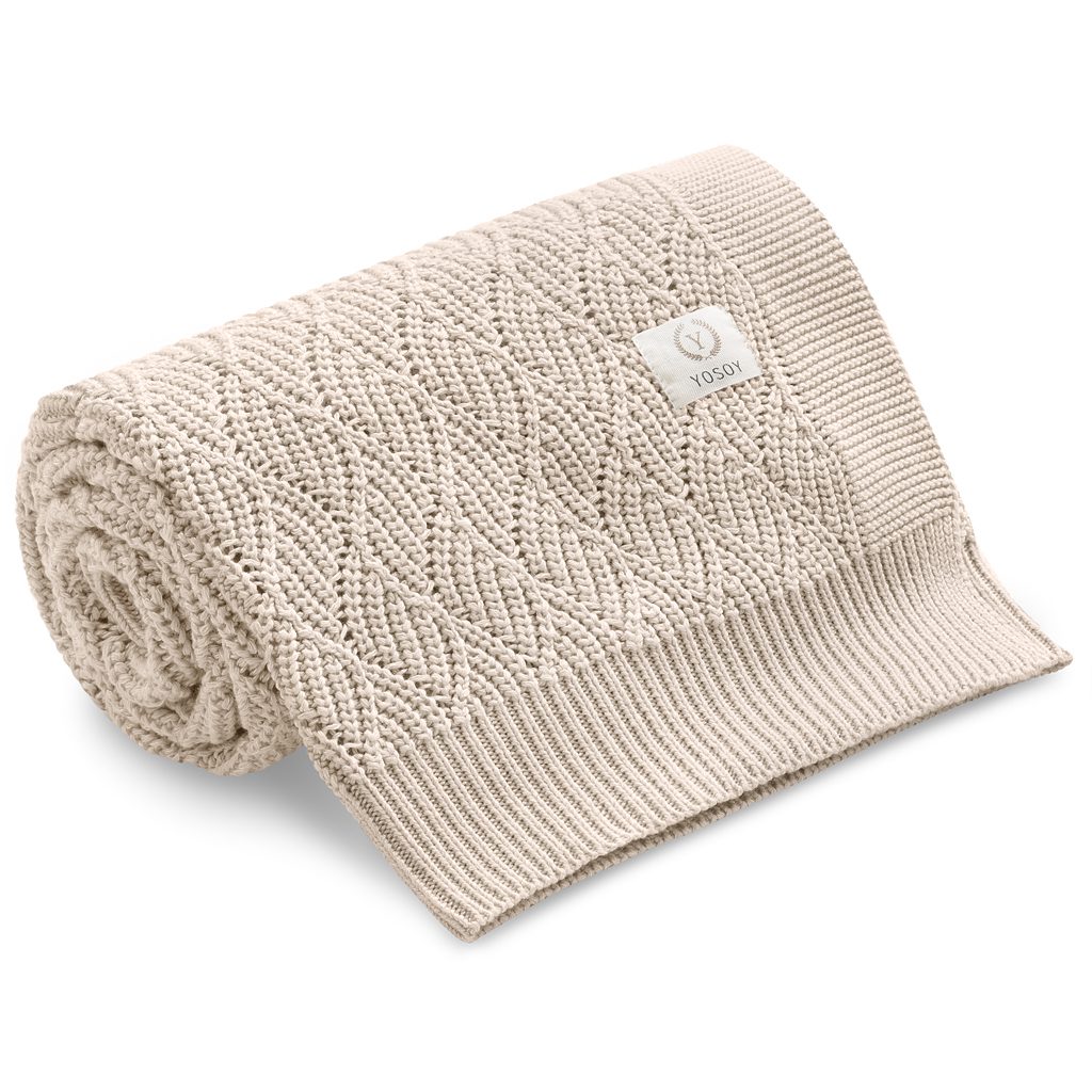 Beżowy kocyk dziecięcy z dzianiny z wzorem, zwinięty i gotowy do użytku.