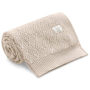 Beżowy kocyk dziecięcy z dzianiny z wzorem, zwinięty i gotowy do użytku.